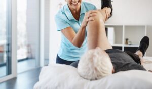 Centro de fisioterapia en Valencia con fisioterapeuta ayudando a un paciente mayor en ejercicio de movilidad de pierna